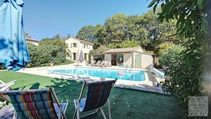 A swimming pool with lounge chairs and a small building, surrounded by greenery.