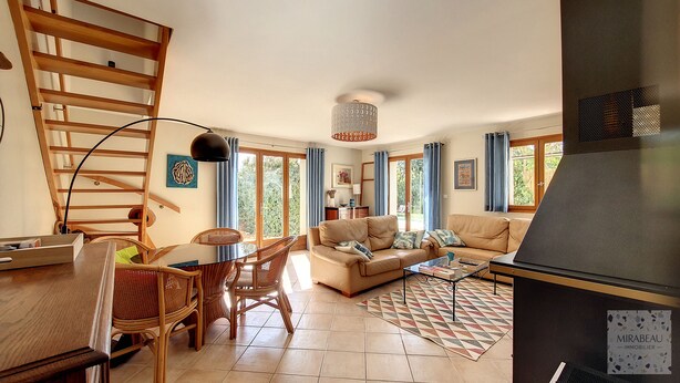 A spacious living area with a high ceiling, a wooden staircase, a dining table with chairs, a sofa, and a coffee table.