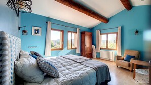 A bedroom with a bed, a chair, a wardrobe, and two windows.