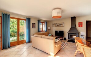 Een woonkamer met een bank, een televisie, een open haard en een eethoek met een stoel.