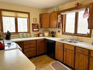 Cocina con armarios de madera, lavavajillas, fregadero y ventana con persianas.