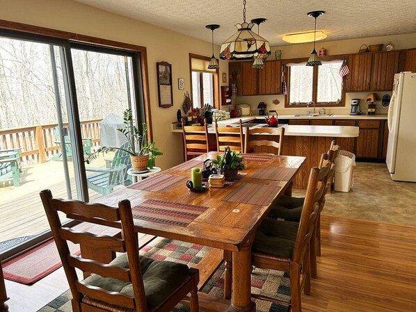 Una mesa de comedor de madera con sillas, una zona de cocina con armarios de madera y un ventanal con vistas a árboles.