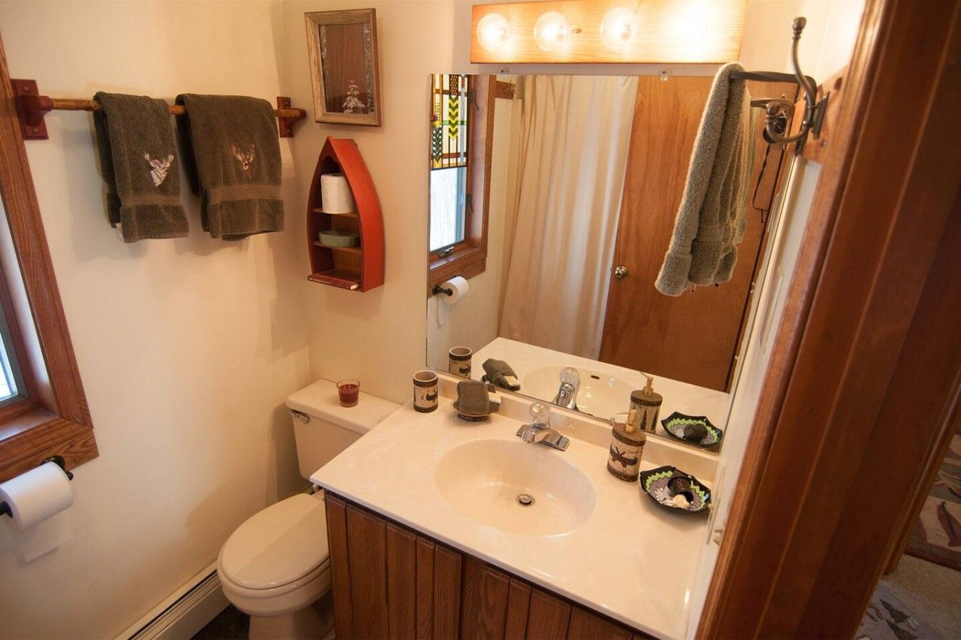 A bathroom with a toilet, sink, and mirror. There are towels hanging on a rack, a soap dispenser, and a glass of water on the sink.