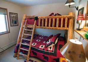 A bunk bed with a ladder, a quilt with bear patterns, a lamp, and a framed picture on the wall.