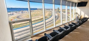 Una habitación con ventanas amplias que dan a una pista de carreras, filas de sillas negras y un cartel de NASCAR.