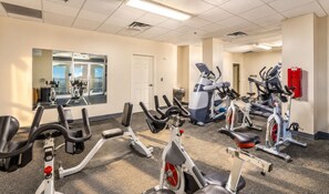 Un gimnasio con equipo de ejercicio diverso, incluyendo bicicletas estáticas, elípticas y cintas de correr.