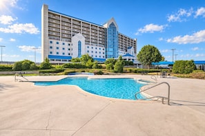 Un hotel con piscina, mobiliario exterior y un edificio grande con varios pisos y balcones.