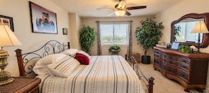 Un dormitorio con cama, cómoda, ventilador de techo y dos plantas en macetas.