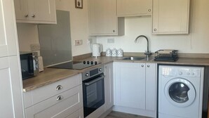 A compact kitchen with white cabinets, a built-in oven, a microwave, a sink, and a washing machine.