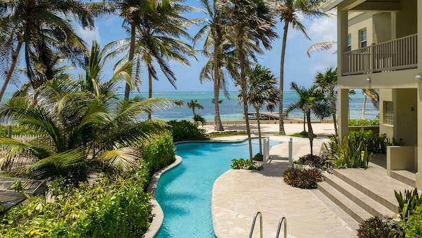 Ein Pool mit gewölbter Kante, umgeben von Palmen und einem Gebäude mit Balkon.