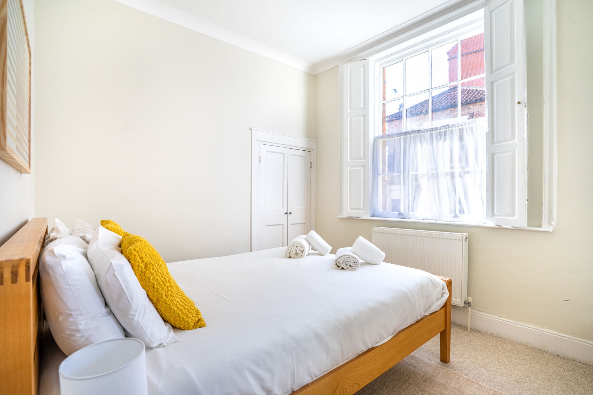 A bedroom with a bed, white walls, a window with curtains, and a radiator.