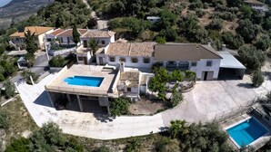 A residential area with a large house featuring a swimming pool, a covered patio, and a hilly backdrop. - Apartment with pool and spectacular views, ideal for families (IZNAJAR)