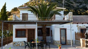 A two-story house with a balcony, a dining area with chairs and a table, and a stone wall. - Apartment with pool and spectacular views, ideal for families (IZNAJAR)