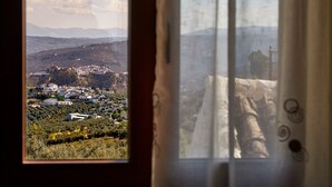 A view through a window with a curtain, featuring a town with buildings and hills in the background. - Apartment with pool and spectacular views, ideal for families (IZNAJAR)