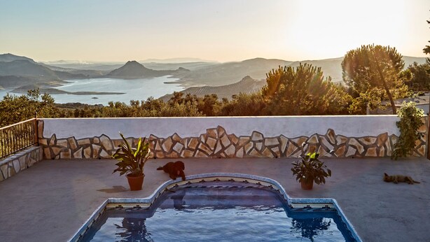 A swimming pool with a stone wall and potted plants, overlooking a scenic landscape with mountains and a body of water. - Apartment with pool and spectacular views, ideal for families (IZNAJAR)