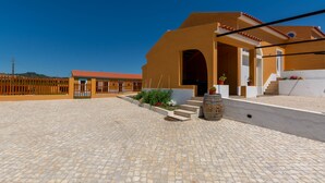 A courtyard with cobblestone flooring, a wooden fence, and a building with a red-tiled roof.