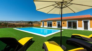 A swimming pool with artificial grass, yellow lounge chairs, and a large umbrella.