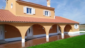 A two-story house with a tiled roof, a covered porch with arches, and a well-maintained lawn.