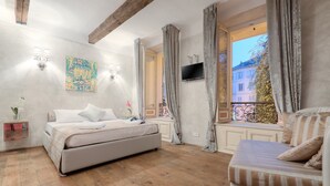 Un dormitorio con una cama grande, un sofá, un televisor y una ventana con cortinas.