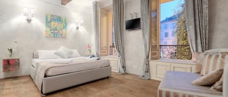 A bedroom with a large bed, a sofa, a TV, and a window with curtains.
