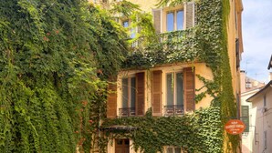 Un edificio de varios pisos con muros cubiertos de hiedra y contraventanas de madera, que muestra un letrero que dice 'L&B Cramères de Thés Bisson'.