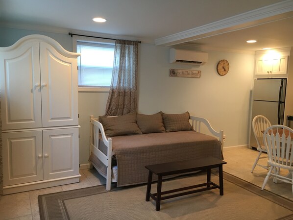 A bedroom with a bed, a wardrobe, a window with curtains, a wall clock, and a refrigerator. - Cozy Studio in Long Beach / EAB (East Atlantic Beach)