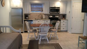 A compact kitchen with white cabinets, a refrigerator, a microwave, and an oven. There is a dining table with chairs and a small rug on the floor. - Cozy Studio in Long Beach / EAB (East Atlantic Beach)