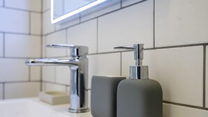 Moderni kylpyhuone, jossa on krominen hana, saippua-annostelija ja peili pesualtaan yläpuolella.