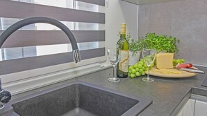 A kitchen with a modern faucet, a wine bottle, glasses, and a cheese board with grapes and a knife. - Natascha in Pamići (Haus für 6 Personen) (Žminj)