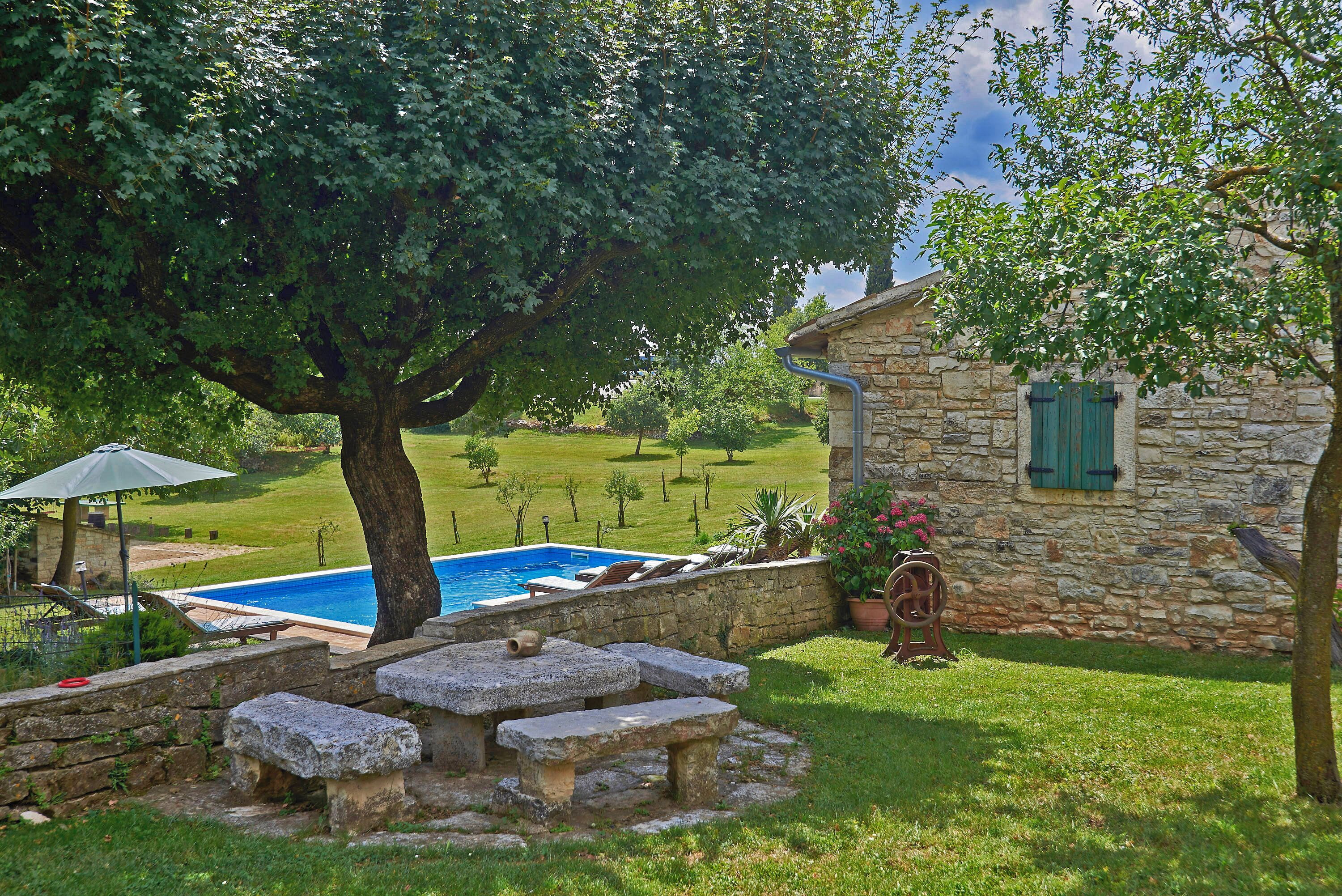 A stone house with a swimming pool, surrounded by a well-maintained lawn and trees.