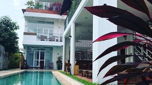 A modern building with a pool, a covered outdoor seating area, and a balcony with plants. - Koki Tree (Siem Reap)