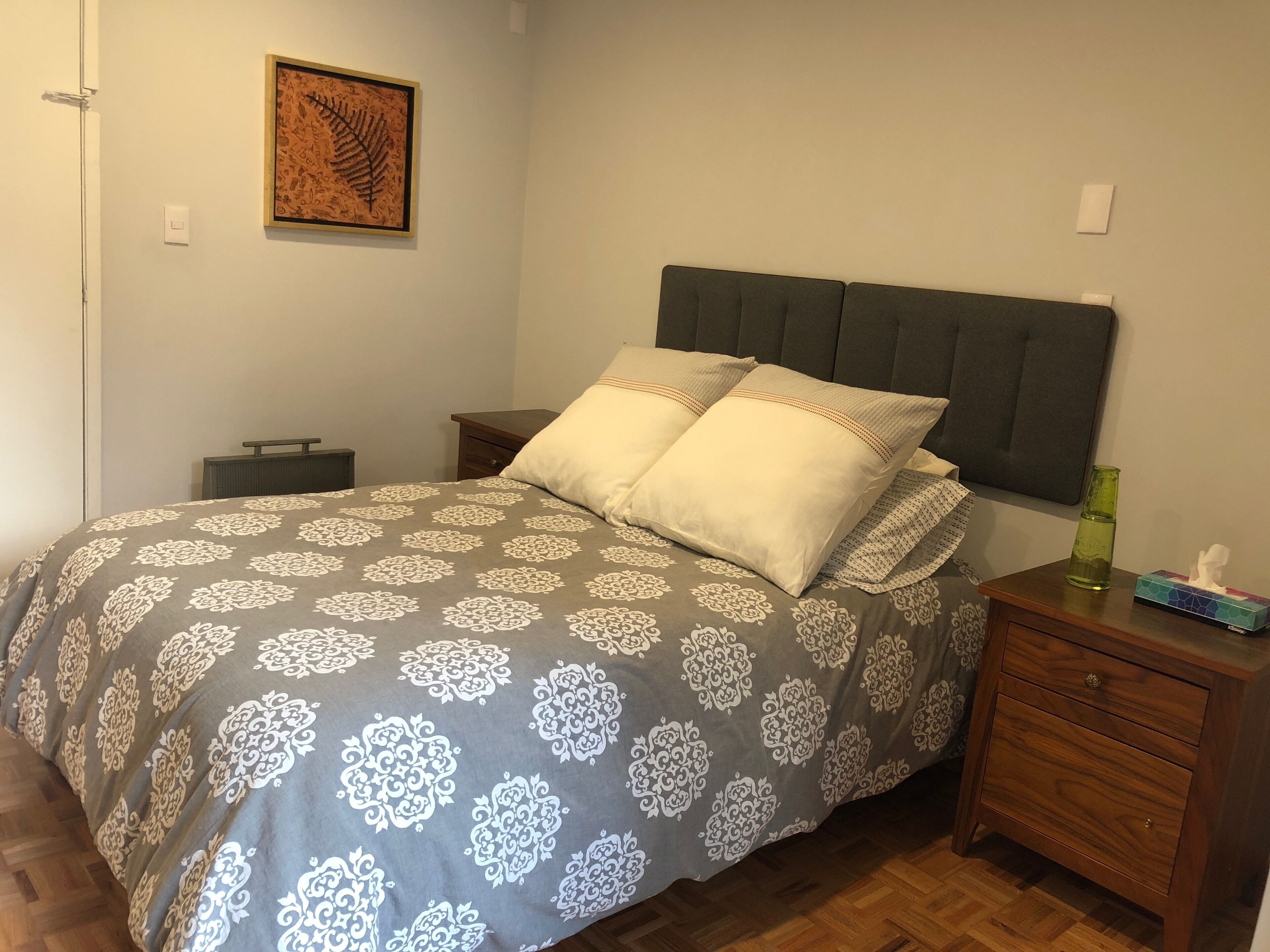 A neatly arranged bedroom with a bed, nightstands, a drawer, and a framed artwork on the wall.