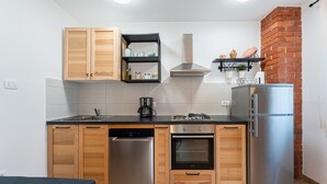 Una cocina compacta con armarios de madera, un refrigerador de acero inoxidable, un horno integrado y una cafetera.