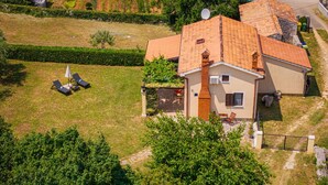 Vista aérea de una casa con techo de tejas, un pequeño jardín con césped y algunas zonas de estar al aire libre.