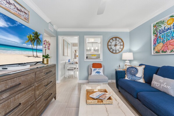 A living room with a view of the beach, a sofa, a coffee table, and a TV on a wooden cabinet.