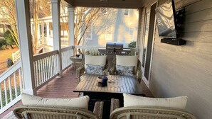 En inglasad veranda med möbler i rotting, en grill och en tv som är monterad på väggen.