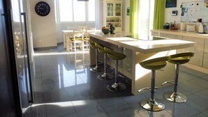 A modern kitchen with a central island, bar stools, a refrigerator, and a dining area with chairs and a table. - luxury villa for 8 persons with private pool, panoramic views, WIFI (Manilva)