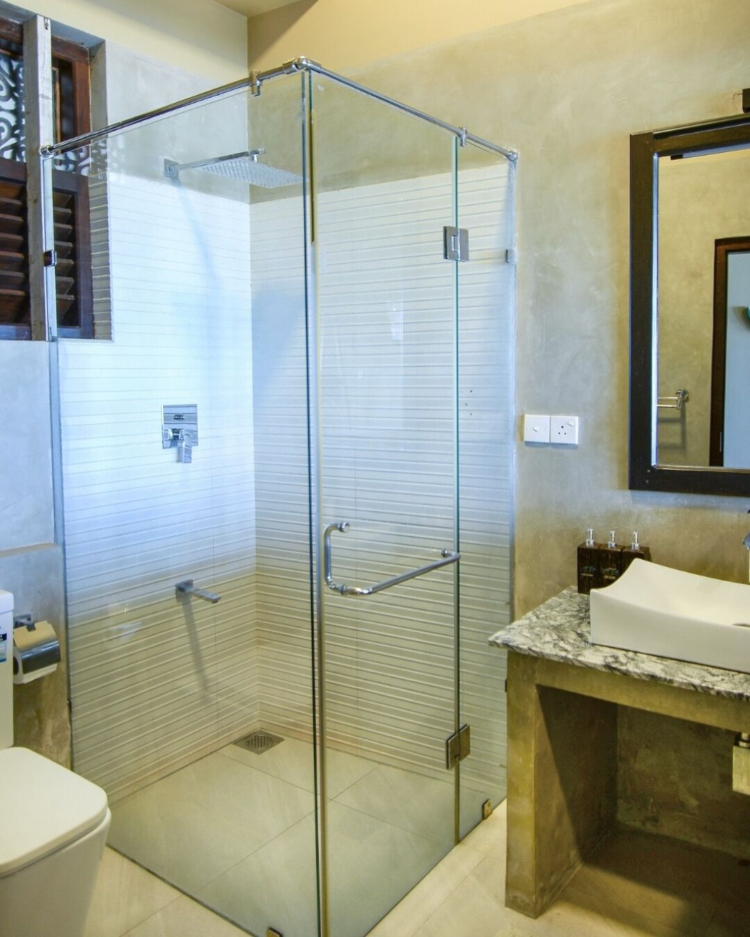 A bathroom with a glass-enclosed shower, a marble sink, and a toilet.