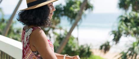 A person leaning on a balcony railing overlooking a beach with palm trees and the ocean.