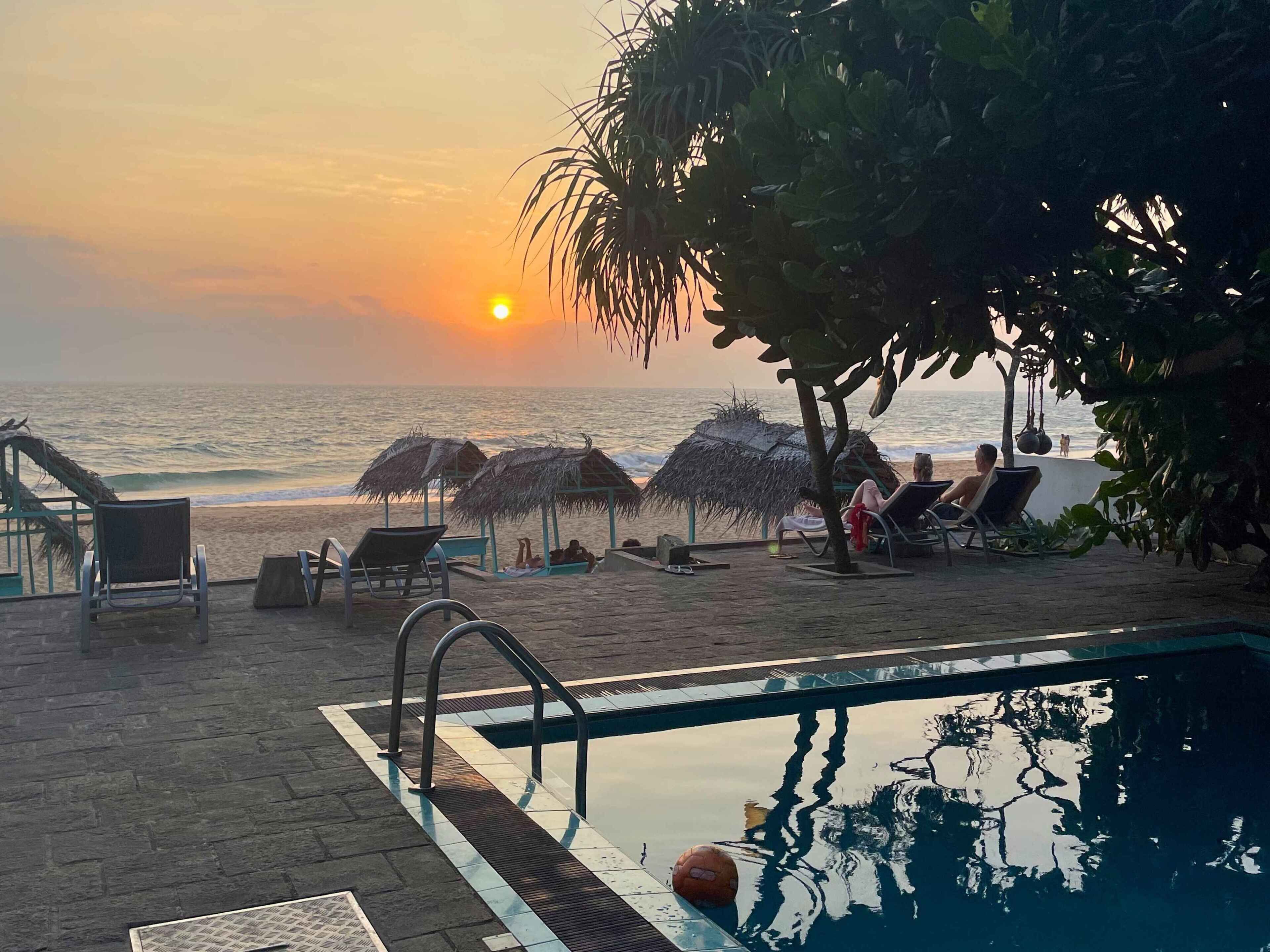 A poolside area with lounge chairs and a pool, overlooking the ocean at sunset.