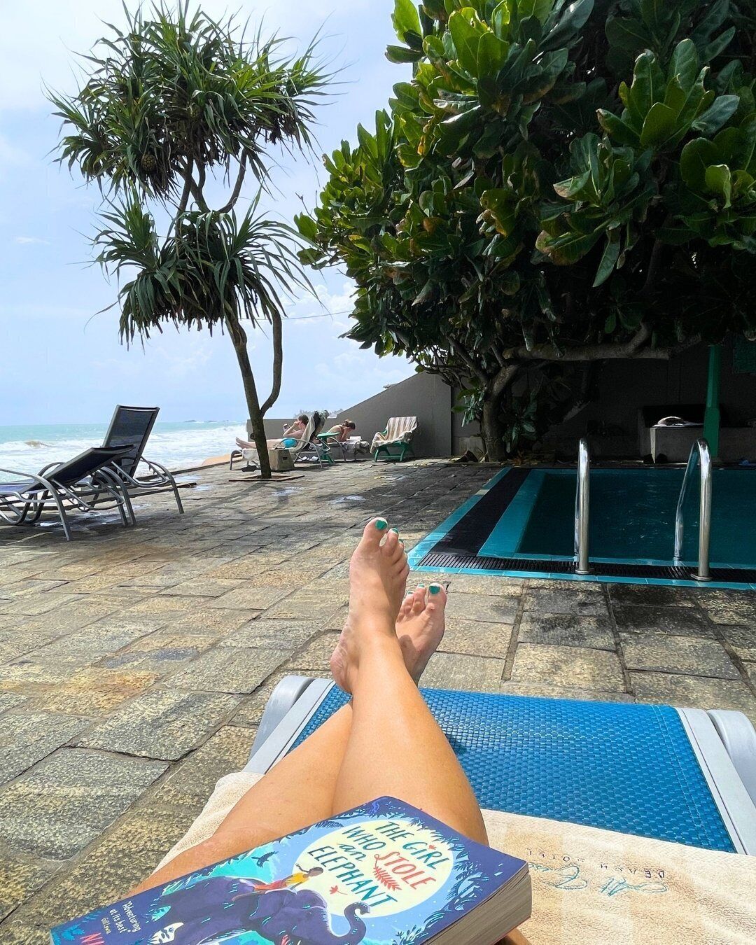 Área na beira da piscina com espreguiçadeiras, piscina e vista para o oceano.