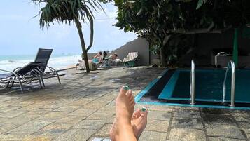 Área na beira da piscina com espreguiçadeiras, piscina e vista para o oceano.