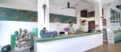 Un mostrador de recepción con dos empleados, un ventilador de techo, obras de arte en las paredes y una pared de acento verde.