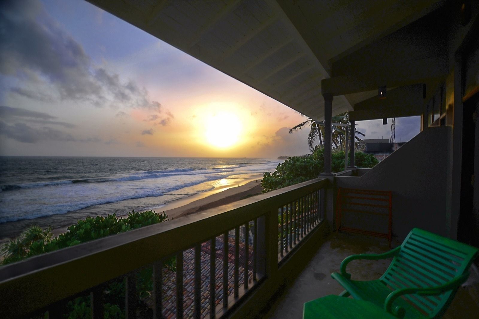 Ein Balkon mit Blick auf das Meer bei Sonnenuntergang, ein grüner Stuhl und ein Geländer.