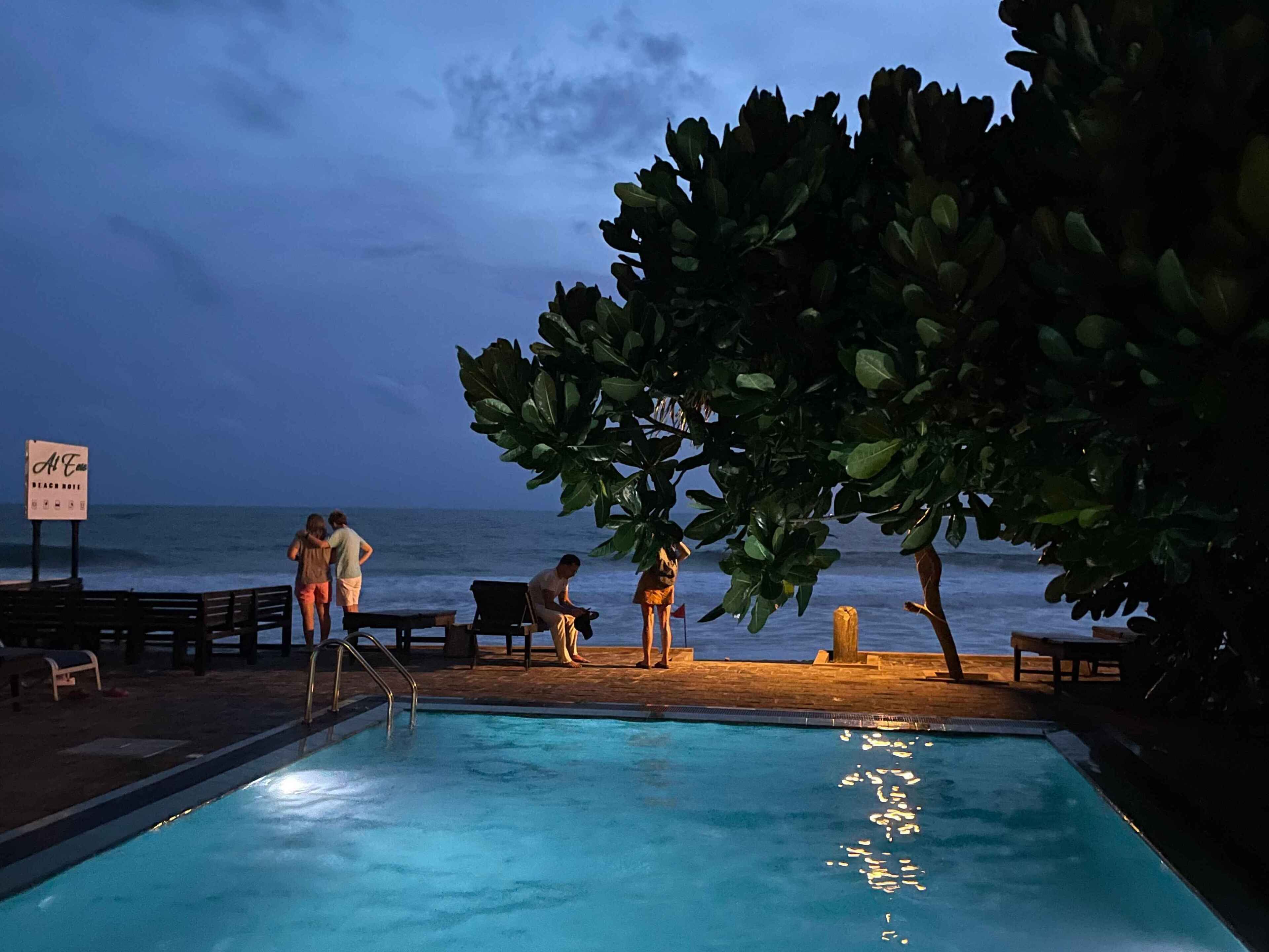 A pool area with a view of the ocean, surrounded by lounge chairs and a signboard.