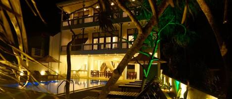 Un hotel de varios pisos con piscina, mobiliario exterior y un área de balcón bien iluminada.