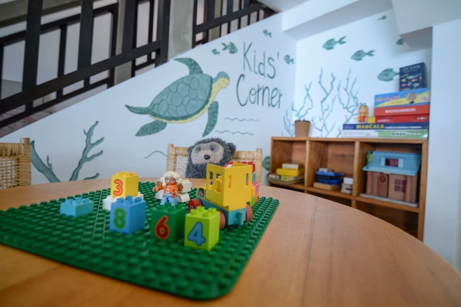 A children's play area with a LEGO play mat, a bookshelf, and a wall mural.