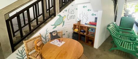 A children's play area with a wooden table, wicker chairs, and a green bench.