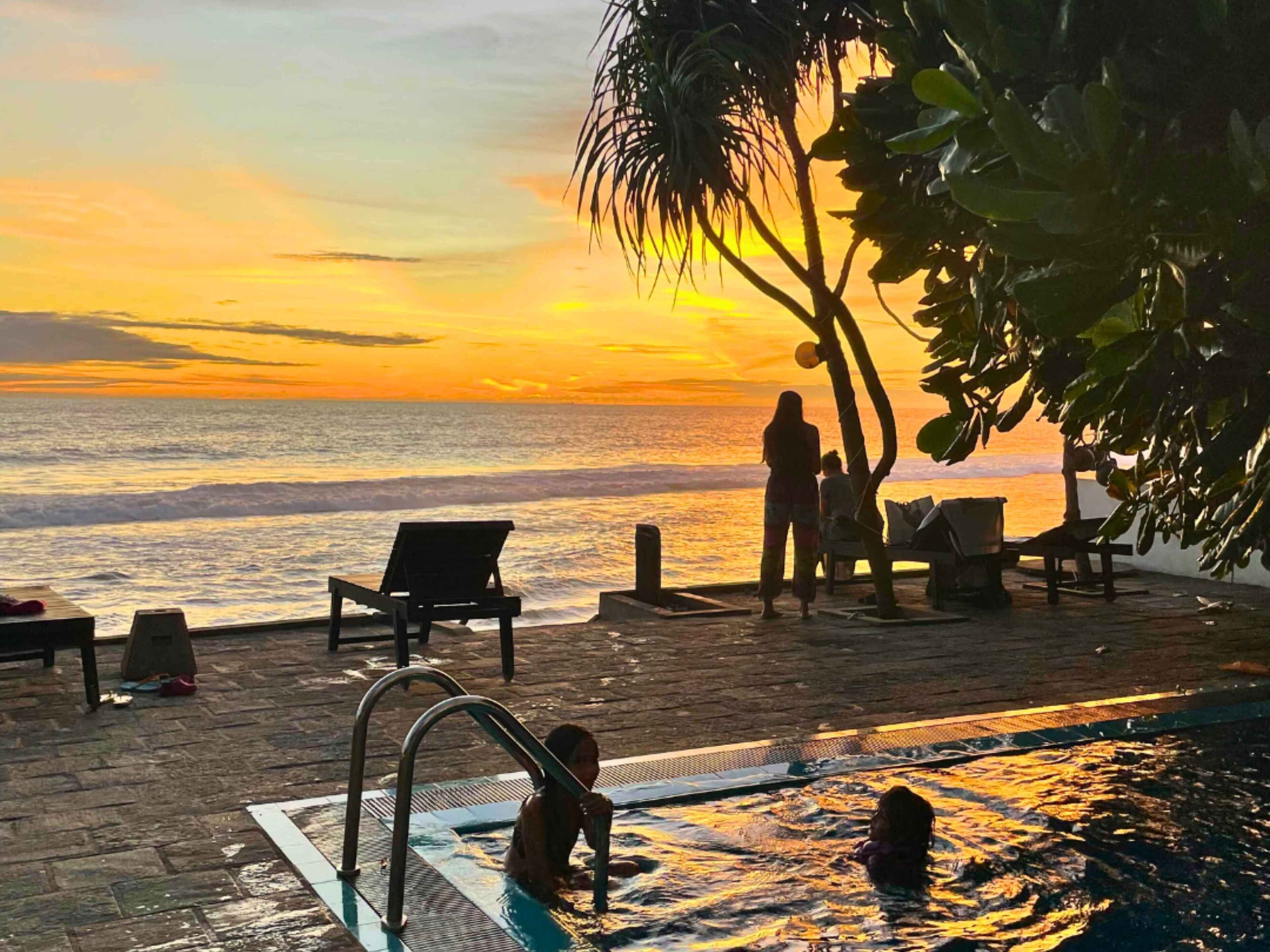 Zona junto a la piscina con vistas a la puesta de sol sobre el océano, sillas de descanso y una piscina pequeña.
