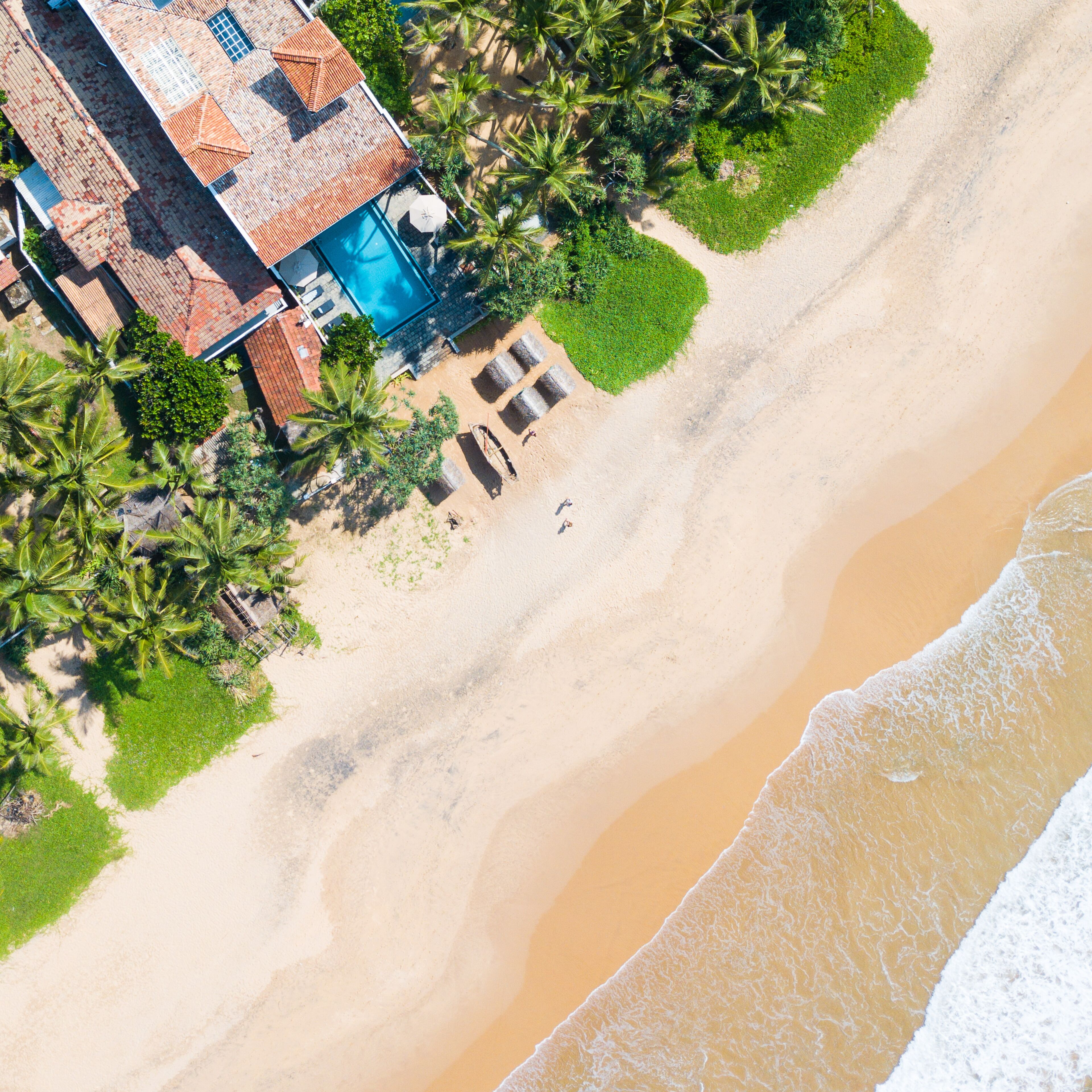 Eine Luftaufnahme eines Anwesens direkt am Strand mit Swimmingpool, Palmen und Sandstrand.